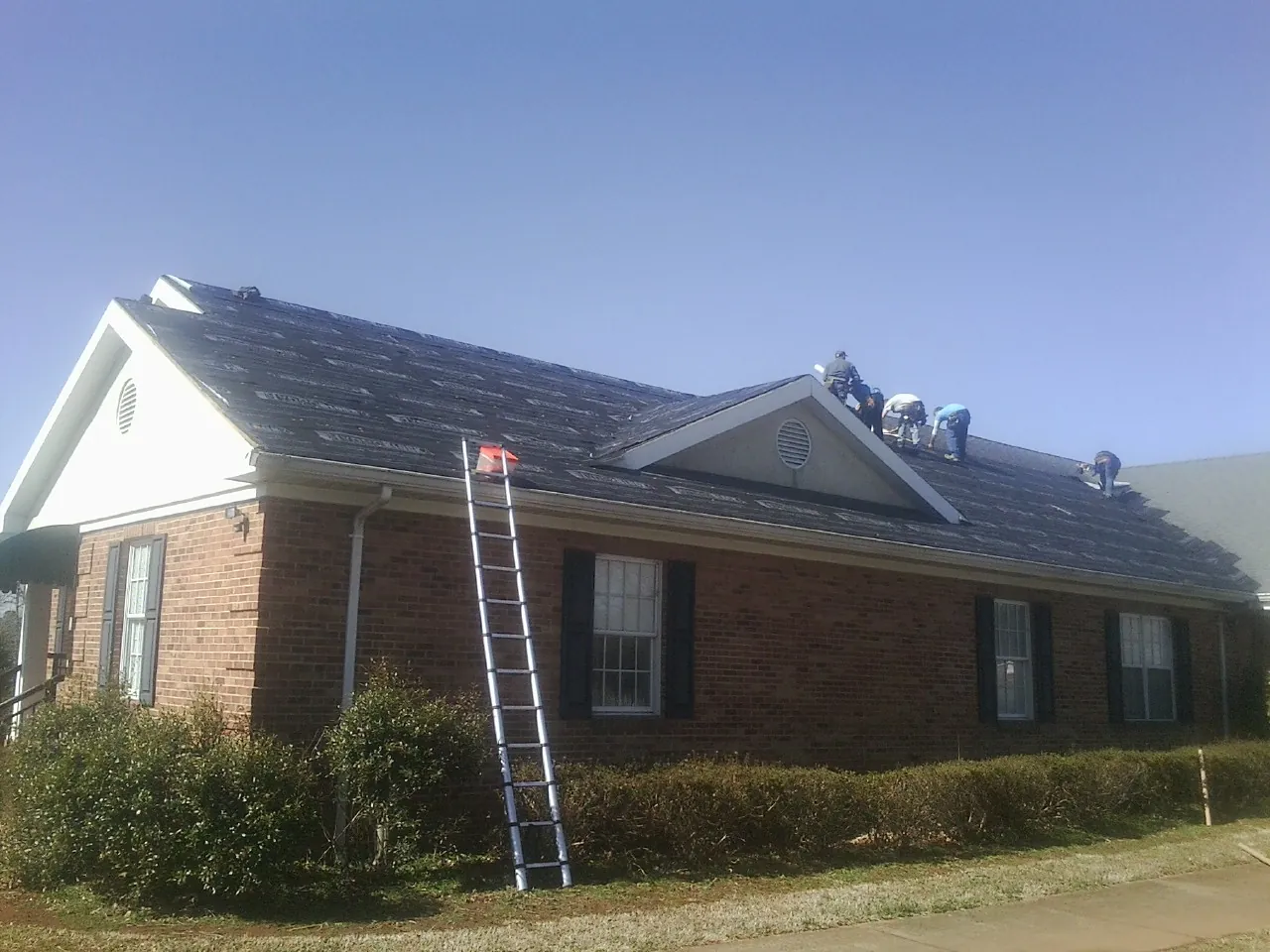 Crew tearing shingles off a brick ranch roof with a ladder set — Metal Roof Repair work by our crew in Parksville