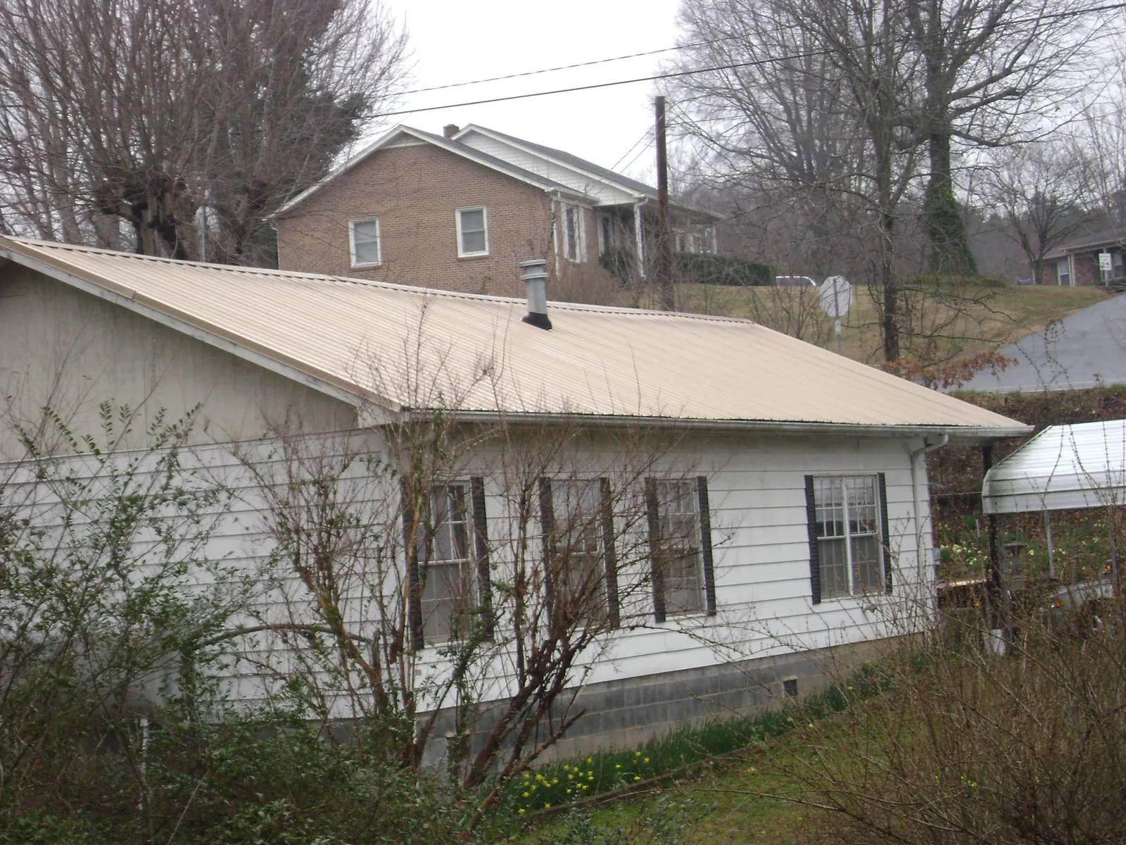 Tan metal roof on a white sided house set into a hillside — Commercial Roofing by Roofing Brothers in Parksville